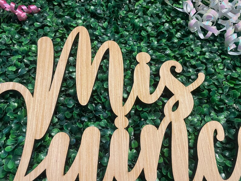 Op de afbeelding: Een lichtbruin houten uitsnede bord met de cursieve tekst Mis Quince. De letters zijn verbonden in een vloeiende schrijfstijl met een zichtbare houtnerftextuur over het gehele oppervlak, wat zorgt voor een natuurlijke en gedetailleerde uitstraling.