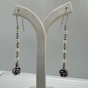 May include: A pair of silver dangle earrings with a rose charm and pearl accents.