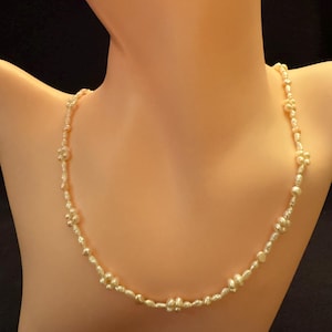 May include: A delicate pearl necklace featuring small, irregularly shaped pearls. The necklace is made of white pearls and is strung on a thin gold chain.