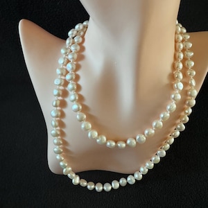 Puede incluir: Un collar de perlas blancas de doble cadena. Las perlas son redondas y tienen un acabado liso y brillante.