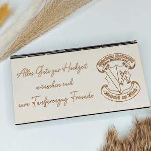 May include: A wooden sign with the text "Alles Gute zur Hochzeit" and "eure Fanfarenzug Freunde" in a cursive font. The sign also features a crest with the text "M&uuml;nchner Fanfarenzug" and "Mittenwald 1924" in a traditional font.