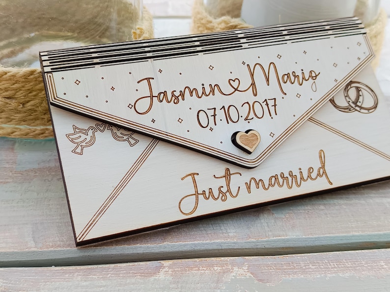 May include: White wooden envelope with the text "Jasmin & Mario 07.10.2017 Just married" and a small heart design.