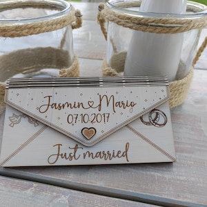 May include: A wooden wedding card shaped like an envelope with the text "Jasmin & Mario 07.10.2017 Just married" and a small heart.