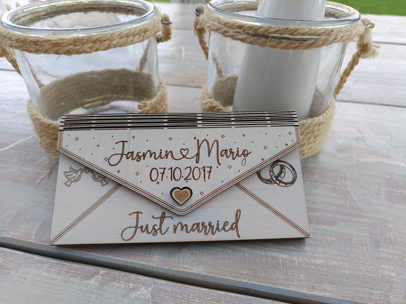 May include: A wooden wedding card shaped like an envelope with the text "Jasmin & Mario 07.10.2017 Just married" and a small heart.