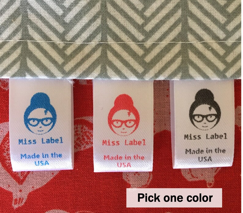 May include: Three white fabric clothing labels with a gray herringbone pattern above. Each label features a graphic of a person with glasses and a bun, the text Miss Label, and the text Made in the USA in blue, red, or black ink respectively.