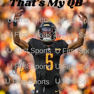 May include: A football player in a black and gold uniform with the number 5, celebrating with arms raised. The image includes the text "That's My QB" and "2024 ROOKIE OF THE YEAR". The background is blurred.