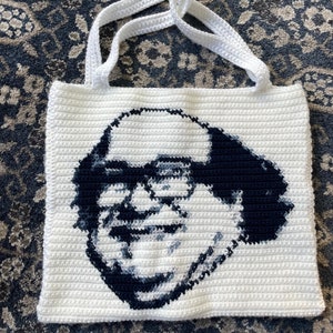 May include: White crocheted tote bag with a black and white image of a man with glasses and a mustache.