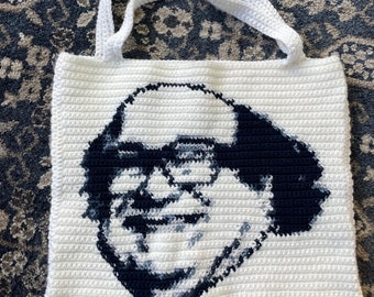 May include: White crocheted tote bag with a black and white image of a man with glasses and a mustache.