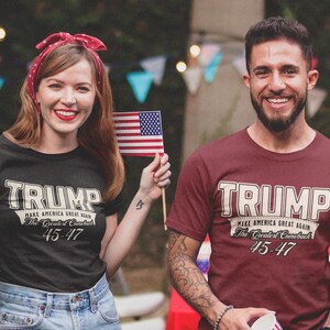 May include: Two people wearing t-shirts with the text "TRUMP MAKE AMERICA GREAT AGAIN The Greatest Comeback 45-47". The person on the left is wearing a black t-shirt and the person on the right is wearing a maroon t-shirt.