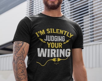 May include: A man wearing a black t-shirt with the text "I'm silently judging your wiring" in white with a yellow lightning bolt and plug graphic.