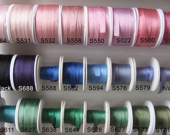 Puede incluir: Primer plano de carretes de cinta en varios colores, incluyendo rosa, negro, azul, verde y gris. Los carretes están etiquetados con números, como "S564", "S688" y "S588".