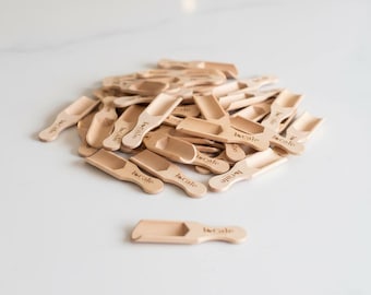 May include: A collection of small, light-colored wooden scoops, each with a small, rectangular bowl and a handle. The word "locale" is printed on each scoop. The scoops are scattered on a white surface.