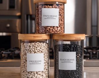 May include: Three glass jars with bamboo lids, each filled with different types of beans. The jars are labeled "Pinto Beans," "Lima Beans," and "Black Beans." The labels also include "Beans & Legumes."
