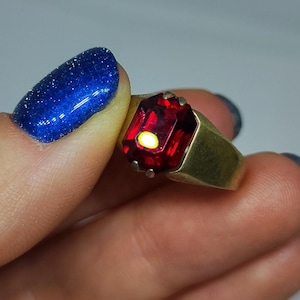 Könnte beinhalten: Ein goldener Ring mit einem großen, roten, smaragdgeschliffenen Edelstein.