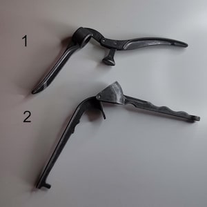 May include: Two different styles of garlic presses. The first is a black metal press with a curved handle and a round pressing area. The second is a black metal press with a straight handle and a rectangular pressing area.