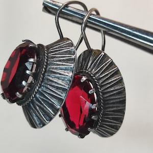 May include: A pair of silver earrings with red gemstone accents. The earrings feature a fan-shaped design with intricate details.
