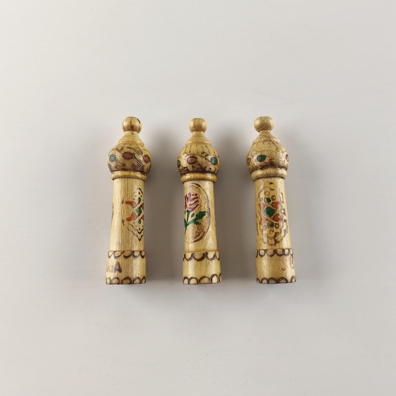 Puede incluir: Tres tapones decorativos de madera para botellas. Cada tap&oacute;n es cil&iacute;ndrico con una parte superior redondeada y dise&ntilde;os pintados intrincados en rojo, verde y dorado. Los tapones miden aproximadamente 15 cm de alto.