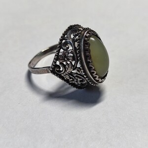 Op de afbeelding: Een zilveren ring met een ovale groene steen gezet in een filigraan ontwerp.