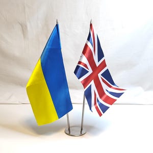 May include: Two small flags on a metal stand. The flag on the left is yellow and blue, the flag on the right is red, white, and blue.