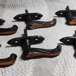May include: Six antique black metal door handles with ornate copper accents. The handles have a decorative design and are in good condition.