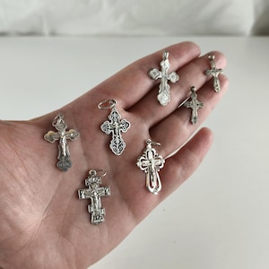 Può includere: Una collezione di ciondoli a forma di croce argentati in vari design. Le croci presentano dettagli intricati e sono esposte su uno sfondo neutro. Alcune croci raffigurano Gesù sulla croce, altre hanno motivi floreali ornati.