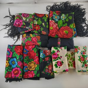 May include: An assortment of colorful floral scarves. The scarves feature vibrant red, pink, blue, and yellow flowers on black and cream backgrounds. Some scarves have black fringe.