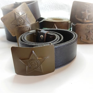 K&ouml;nnte beinhalten: Drei Milit&auml;rg&uuml;rtel mit Metallschnallen, die ein Stern- und Ankerdesign aufweisen. Die G&uuml;rtel sind braun und gr&uuml;n mit einem gewebten Stoffband.