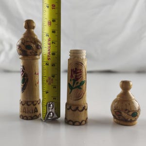 Puede incluir: Tres peque&ntilde;os objetos decorativos de madera tallada a mano. El m&aacute;s alto mide 10 cm de alto, con dise&ntilde;os florales y geom&eacute;tricos pintados. La pieza del medio es un cilindro con una rosa pintada. El m&aacute;s peque&ntilde;o tiene forma redondeada.