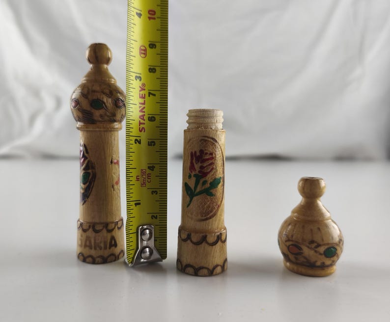 Puede incluir: Tres peque&ntilde;os objetos decorativos de madera tallada a mano. El m&aacute;s alto mide 10 cm de alto, con dise&ntilde;os florales y geom&eacute;tricos pintados. La pieza del medio es un cilindro con una rosa pintada. El m&aacute;s peque&ntilde;o tiene forma redondeada.