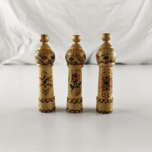 Puede incluir: Tres objetos decorativos de madera tallada a mano. Cada uno tiene una parte superior bulbosa con detalles pintados y un cuerpo cil&iacute;ndrico. Los cuerpos est&aacute;n adornados con dise&ntilde;os florales y geom&eacute;tricos pintados en rojo, verde y dorado. Los objetos miden aproximadamente 13 cm de alto.