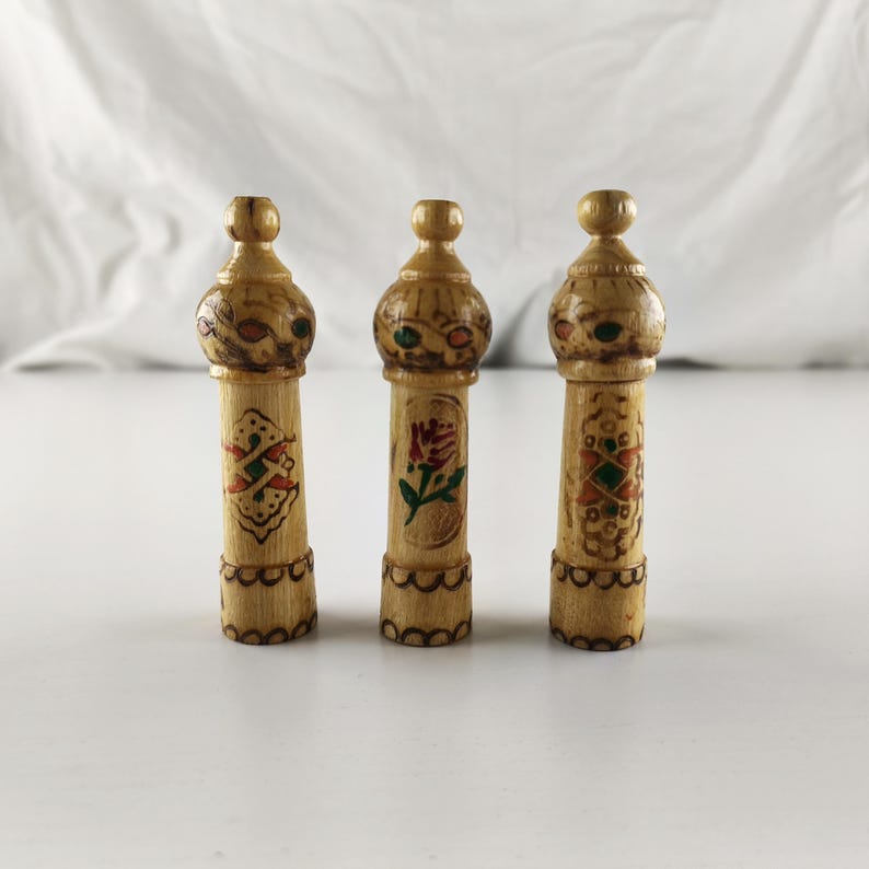 Puede incluir: Tres objetos decorativos de madera tallada a mano. Cada uno tiene una parte superior bulbosa con detalles pintados y un cuerpo cil&iacute;ndrico. Los cuerpos est&aacute;n adornados con dise&ntilde;os florales y geom&eacute;tricos pintados en rojo, verde y dorado. Los objetos miden aproximadamente 13 cm de alto.