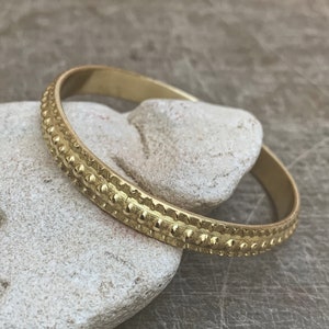 May include: A gold bangle bracelet with a textured, beaded design.