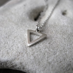 May include: A silver necklace featuring a triangle pendant. The triangle is hollow and has a simple, modern design.