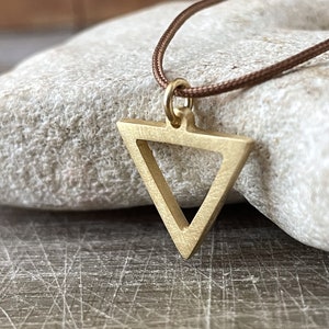 Peut inclure: Un collier avec un pendentif en forme de triangle doré sur un cordon marron. Le triangle a un plus petit triangle à l'intérieur.