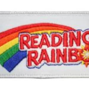 Pode incluir: Um patch retangular branco com um arco-íris colorido e as palavras "READING RAINBOW" em vermelho, contornadas em azul. O arco-íris se estende da esquerda para a direita, com o texto e um desenho de estrela no centro.