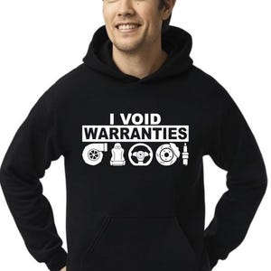 May include: Black hooded sweatshirt with the text "I Void Warranties" in white. Below the text are white illustrations of car parts, including a turbocharger, engine, steering wheel, brake rotor, and spark plug. The person is smiling.