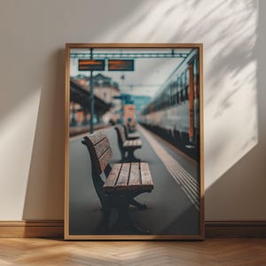 May include: A framed wall art print featuring a perspective view of a train station platform with wooden benches lined up along the tracks. A train is visible on the right side, and a digital information sign hangs above the platform in the distance.