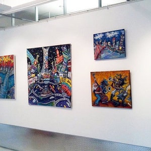 May include: A gallery wall display of colorful, abstract paintings. The paintings feature a variety of subjects, including cityscapes, musicians, and landscapes. The paintings are all framed and hung on a white wall.
