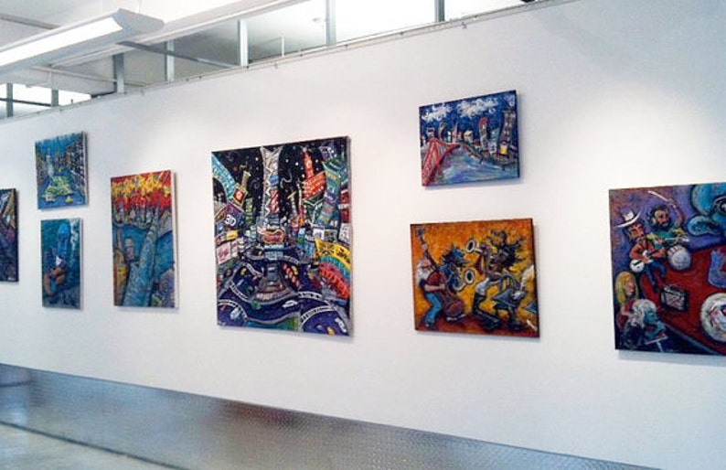 May include: A gallery wall display of colorful, abstract paintings. The paintings feature a variety of subjects, including cityscapes, musicians, and landscapes. The paintings are all framed and hung on a white wall.