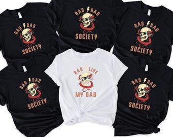 May include: Black and white t-shirts with a skull graphic and the words "RAD DAD SOCIETY". One white t-shirt features the text "RAD LIKE MY DAD". The graphic includes a skull, lightning bolt, and snake.