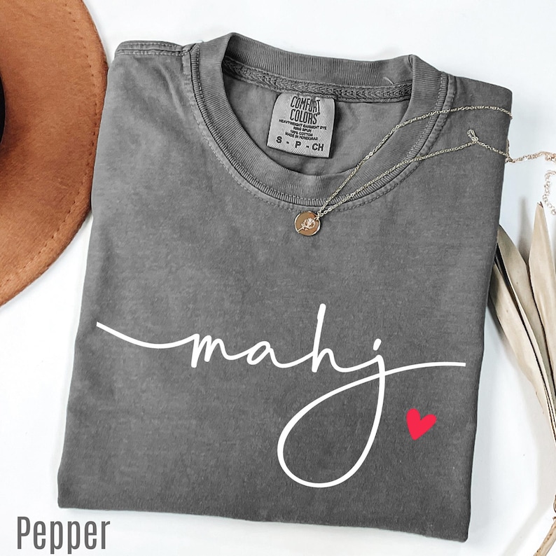 A gray t-shirt with the word "Mahj" written in cursive, a small heart symbol, and a necklace with a pendant.