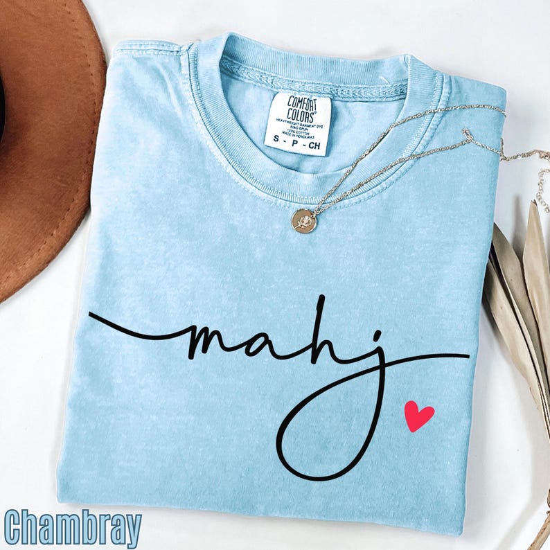 A light blue t-shirt with the word "Mahj" written in cursive, a small heart symbol, and a necklace with a pendant.