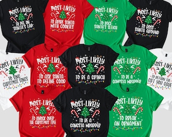 May include: A collection of Christmas-themed t-shirts in various colors, including black, red, green, and white. Each shirt features the phrase "MOST LIKELY" above a Christmas tree graphic and a humorous statement below, such as "TO PEE ON SANTA'S LAP."