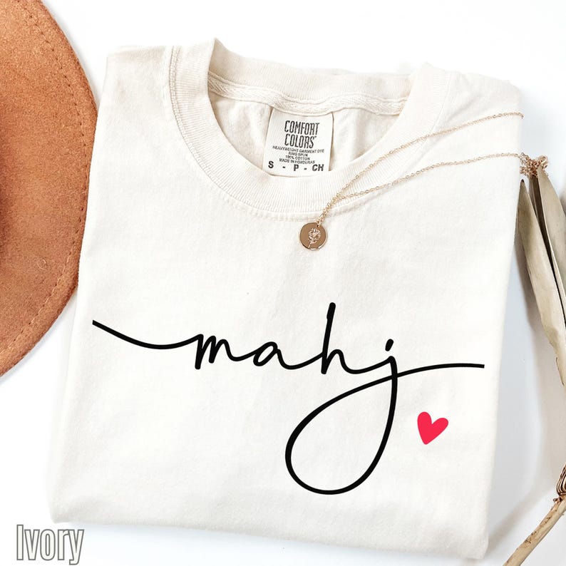 A white t-shirt with the word "Mahj" written in cursive script, along with a small red heart symbol, is displayed on a white background.