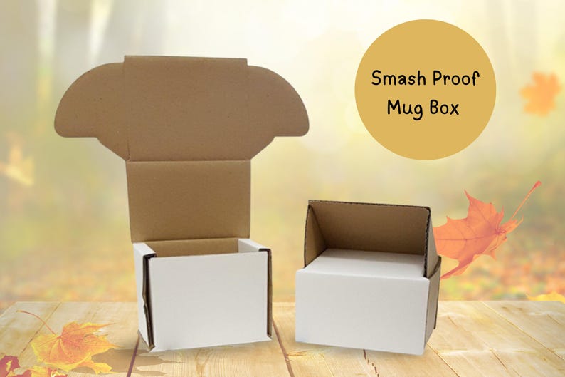 May include: Two white and brown cardboard mug boxes, one open and one closed, are displayed on a wooden surface. The boxes have a simple design with the text "Smash Proof Mug Box" in a yellow circle.