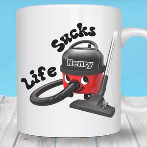 May include: White ceramic mug with a cartoon vacuum cleaner design. The vacuum cleaner is red and black with the name "Henry" on it. The text "Life Sucks" is written above the vacuum cleaner in black.