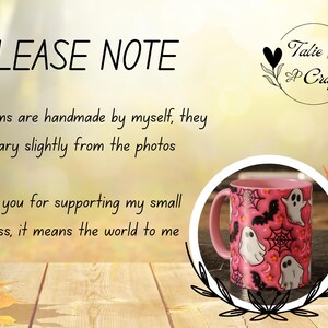 May include: Pink ceramic mug with a Halloween design. The mug displays white ghost illustrations, black bats, and spiderwebs on a pink backdrop. The mug has a pink handle and the text "PLEASE NOTE" is visible.