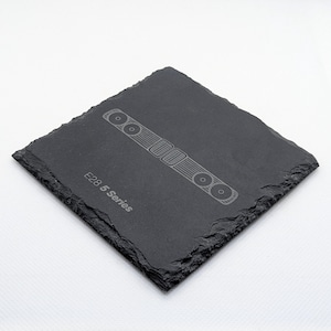 May include: Black slate coaster featuring a white outline of a car grille and the text "E28 5 Series".