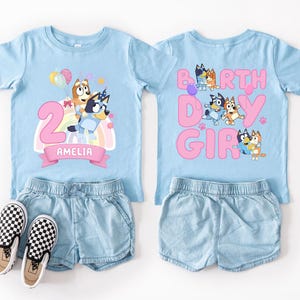 A pair of blue t-shirts with cartoon character designs and the text "Amelia" printed on them, along with denim shorts and checkered shoes.