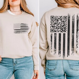 The image is a collage of two photos showing the back of a beige sweatshirt with an American flag design and a QR code printed on the back.
